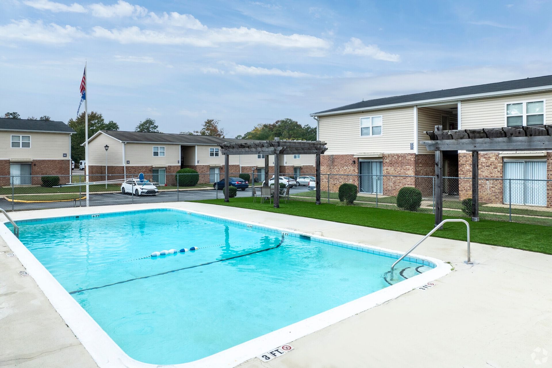 Pool and two-story apartment buildings. Blue pool water, light beige buildings with brick trim. Sunny, daytime.