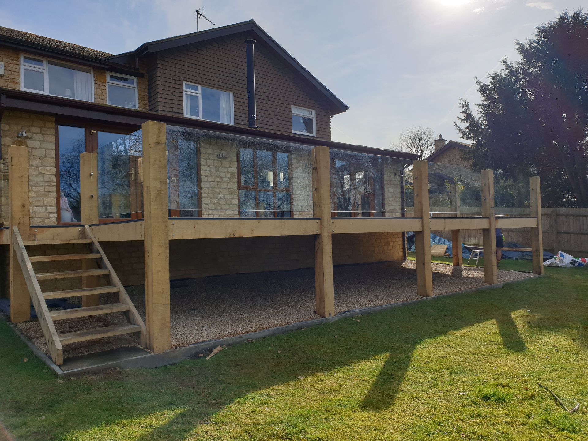 Wooden raised deck with stairs attached to a brick house in a sunny backyard.