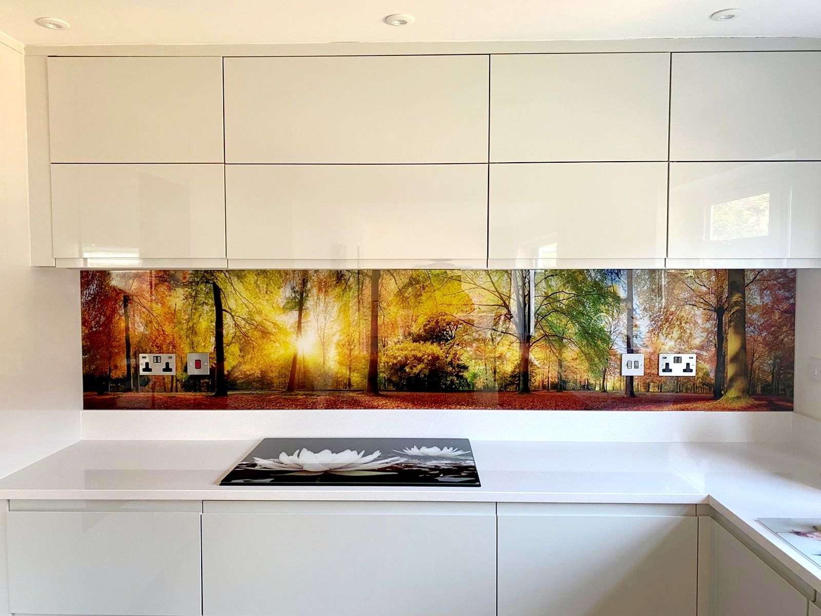 Modern white kitchen with glossy cabinets, forest backsplash, and white countertops