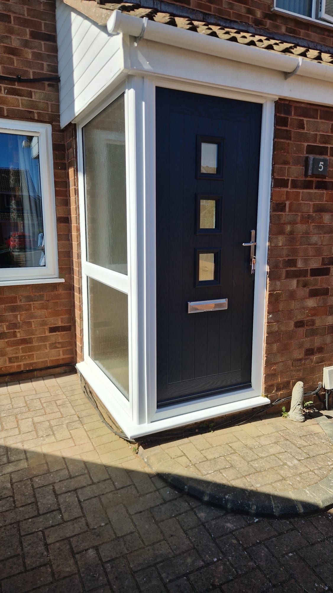 Front entrance with a dark blue door and white enclosed porch on a brick house
