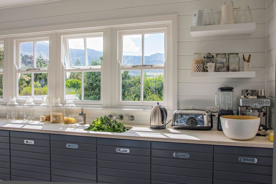 Bright kitchen with white counters, dark cabinets, and windows overlooking greenery and mountains.