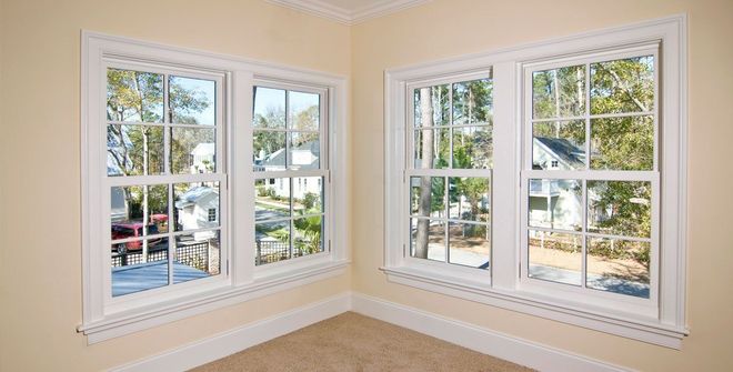 Bright corner room with beige walls and white-trimmed windows overlooking a street and trees.