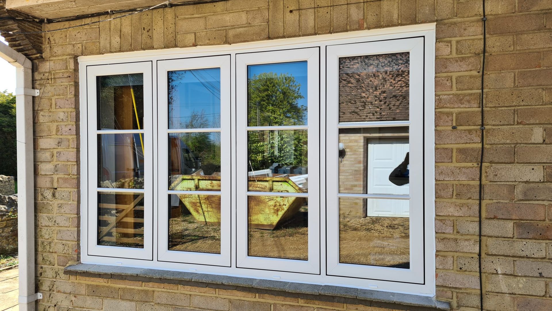 White-framed sliding glass doors set in a tan brick wall reflect trees and a patio.