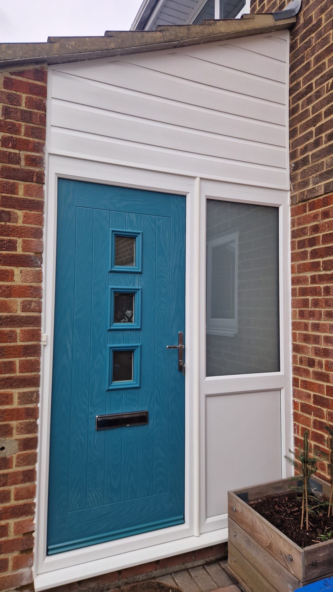 Blue front door with three square windows beside a frosted side panel on a small porch
