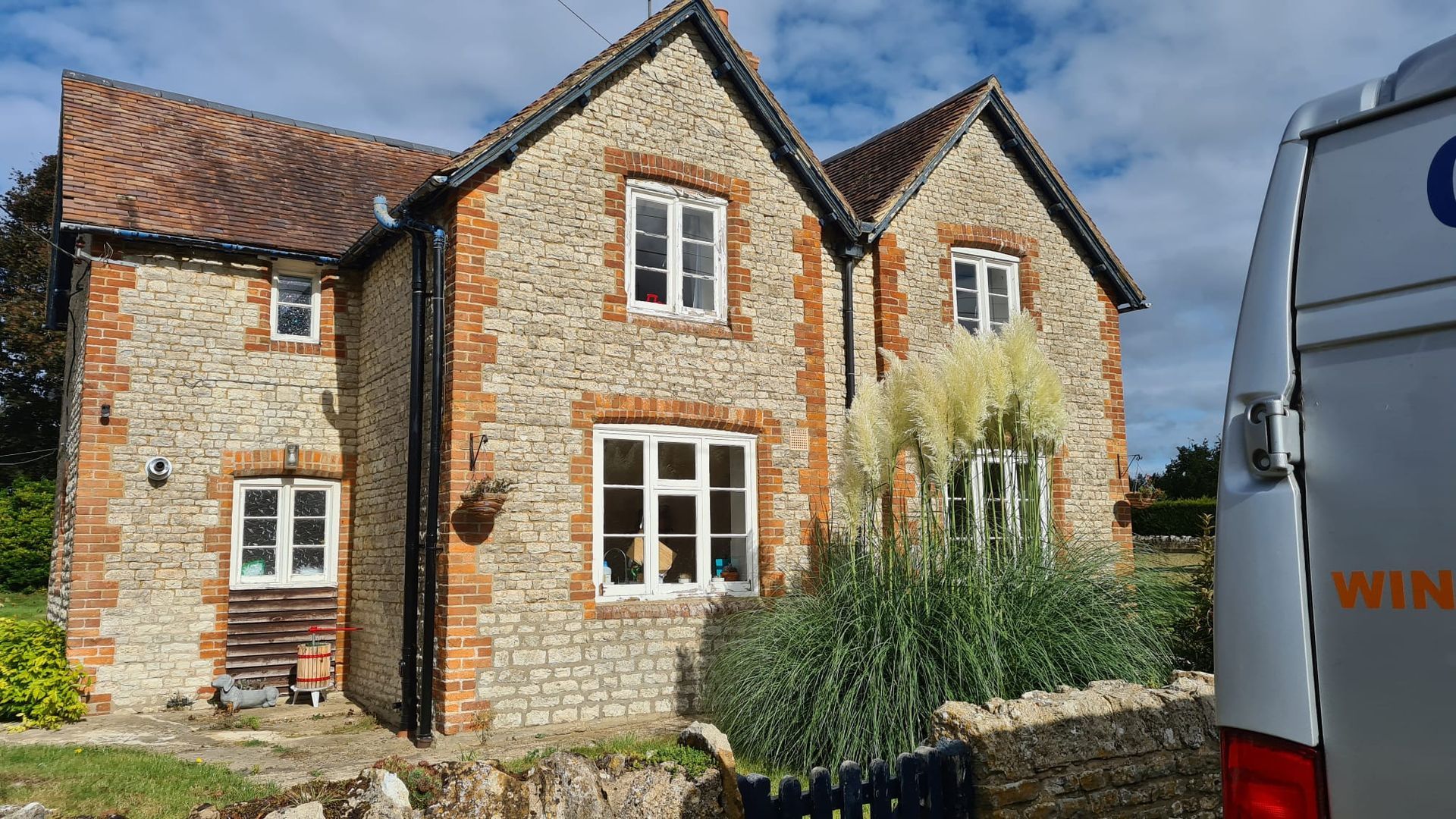 Stone cottage with white-framed windows and ivy, beside a parked white van under a blue sky