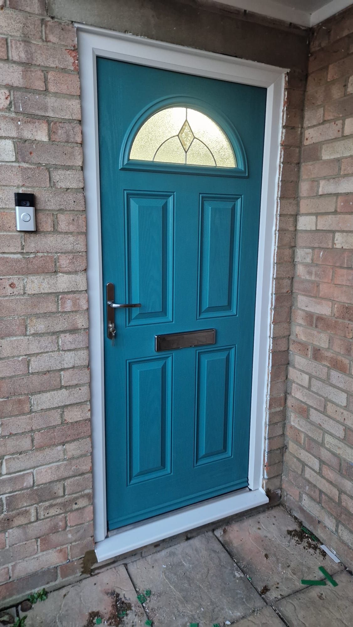 Teal front door with half-moon glass window and mail slot in a brick entryway