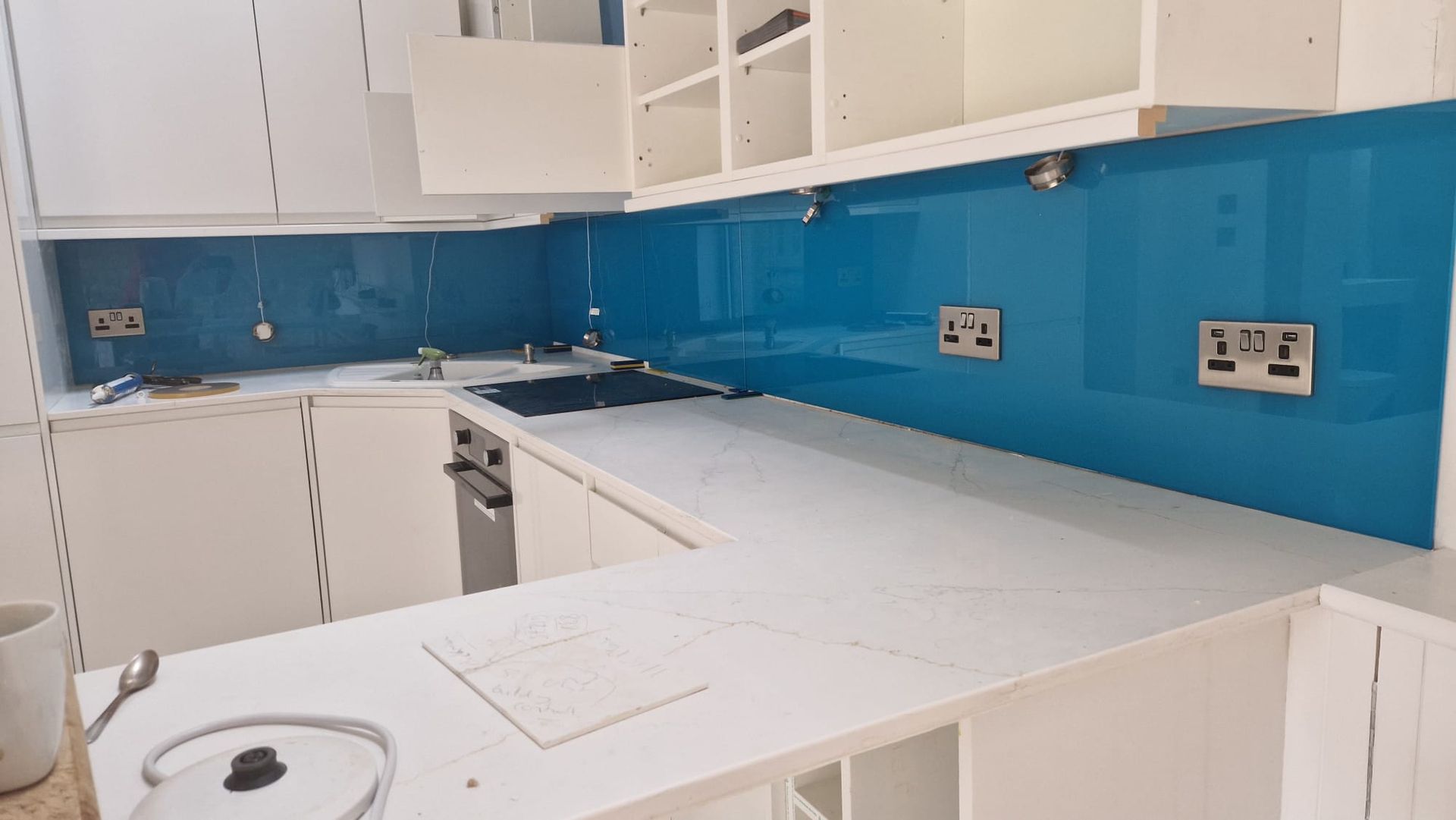 Modern white kitchen under renovation with blue backsplash, unfinished countertops, and exposed cabinets