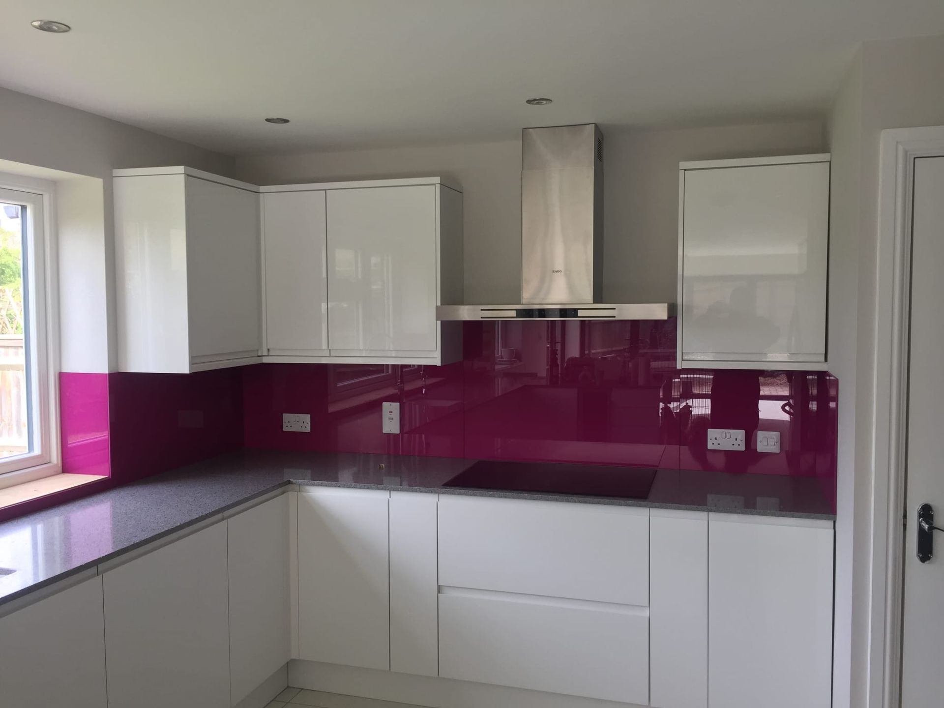Modern kitchen with white cabinets, magenta glass backsplash, gray countertops, and stainless steel range hood