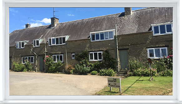 Row of stone cottages with white windows and a sloped roof, set beside a gravel drive and lawn