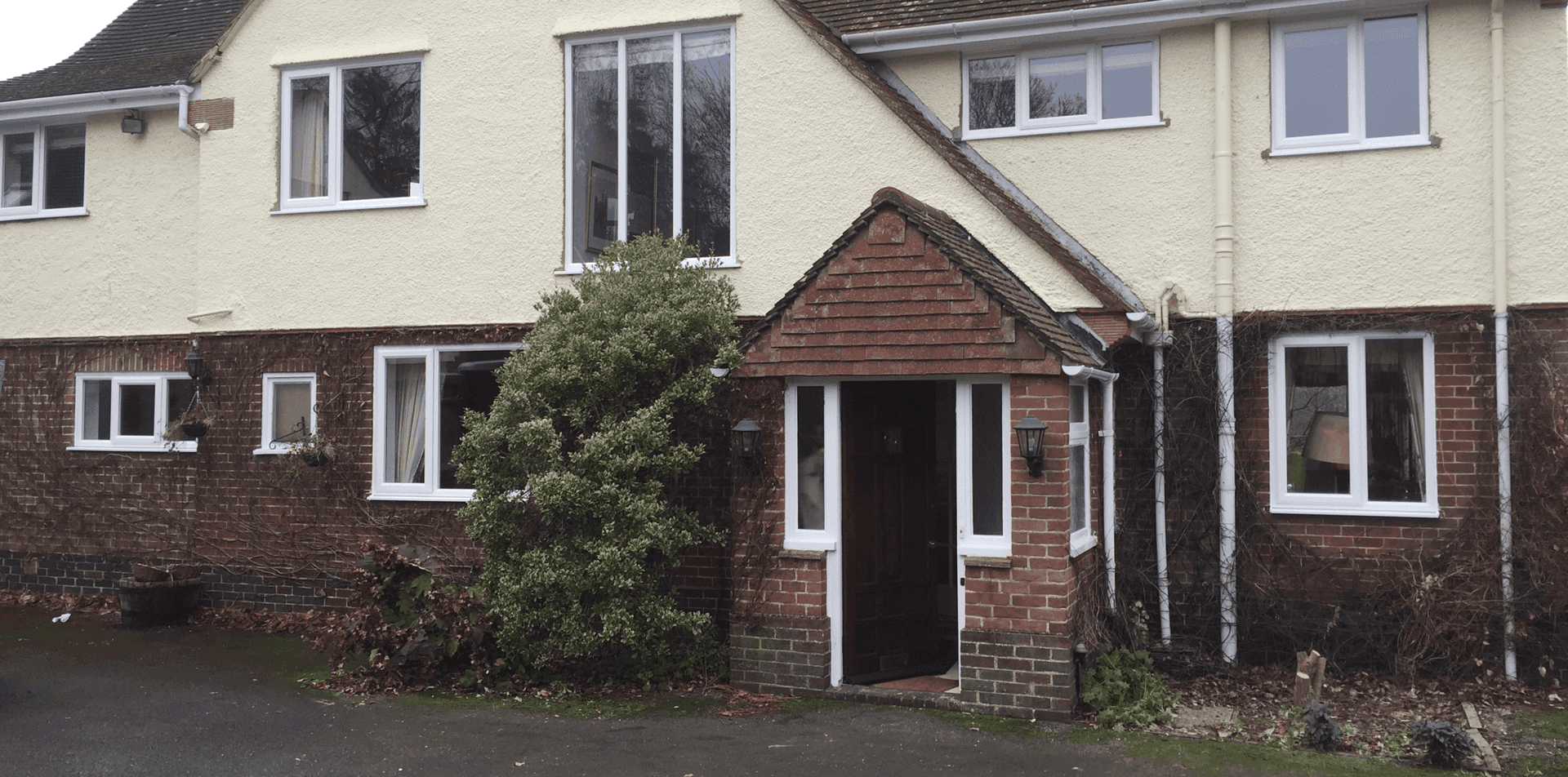 Suburban townhouse exterior with cream walls, brown roof, front door, windows, and wet pavement