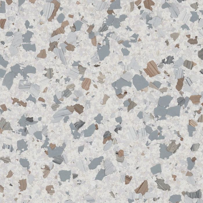 A textured surface pattern featuring light gray, slate blue, and warm tan flecks scattered over a speckled white background.