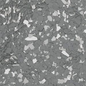A close-up of grey, white, and dark grey paint chips, typical of a decorative epoxy garage floor coating.