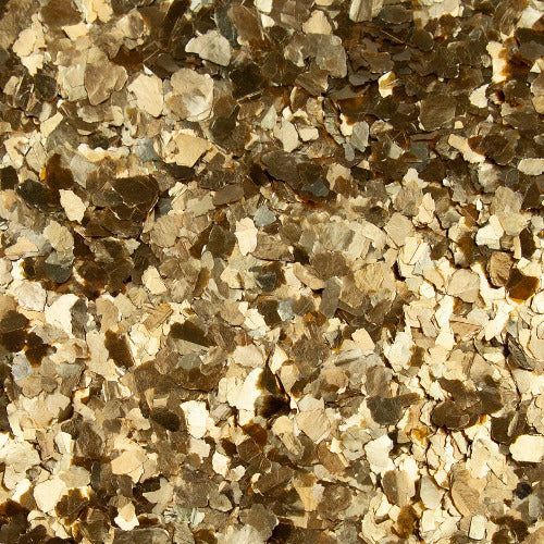 A close-up texture of small, irregular flakes in varying shades of beige, tan, and dark brown.