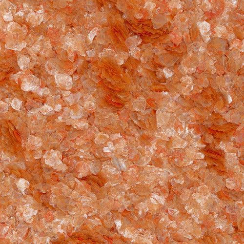 A close-up of coarse, translucent orange-pink Himalayan salt crystals.