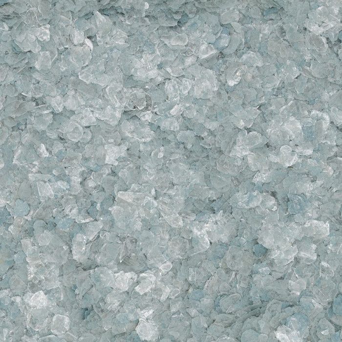A close-up view of small, translucent, pale blue crushed glass or salt crystals filling the frame.