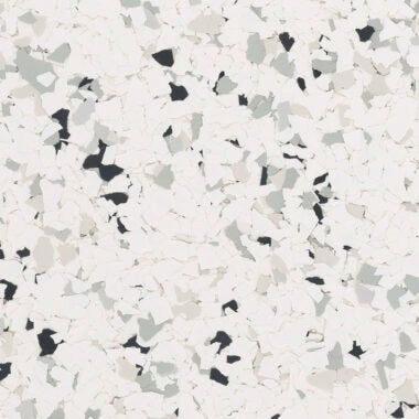 A close-up of a speckled floor coating with white, grey, and black flakes over a light-colored base.