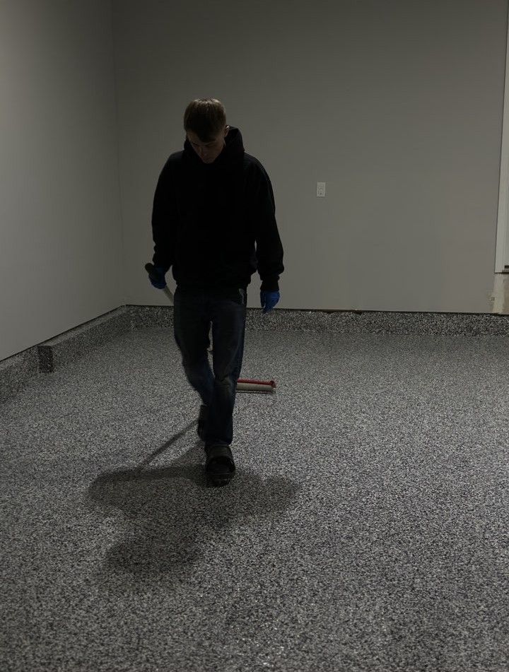 A person in a dark hoodie and jeans stands in a room with a finished gray speckled epoxy garage floor.