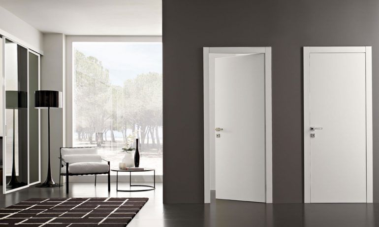 Stanza moderna e minimalista con due porte bianche, uno specchio, una sedia, una lampada e una grande finestra con vista sugli alberi
