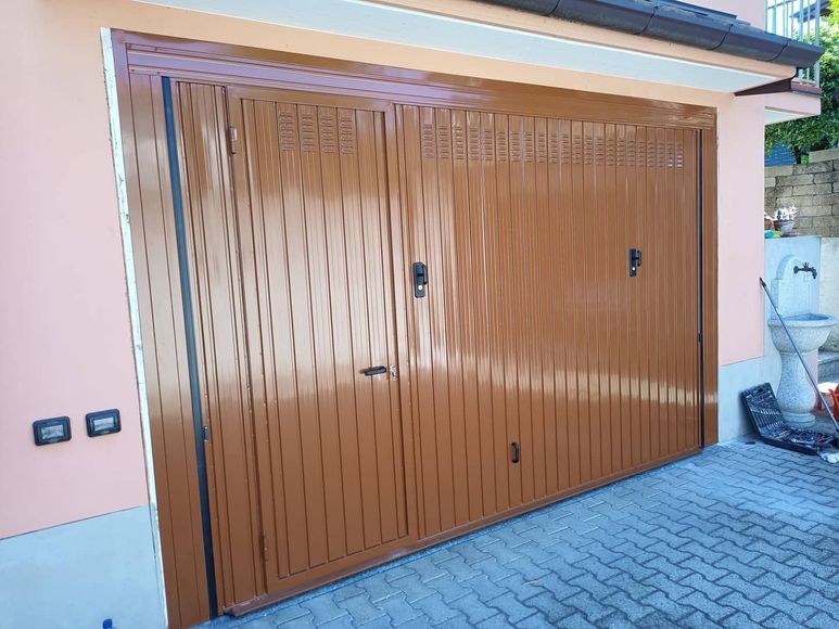 Porta del garage in legno marrone con pannelli superiori a listelli, sulla facciata di una casa, accanto a un vialetto pavimentato