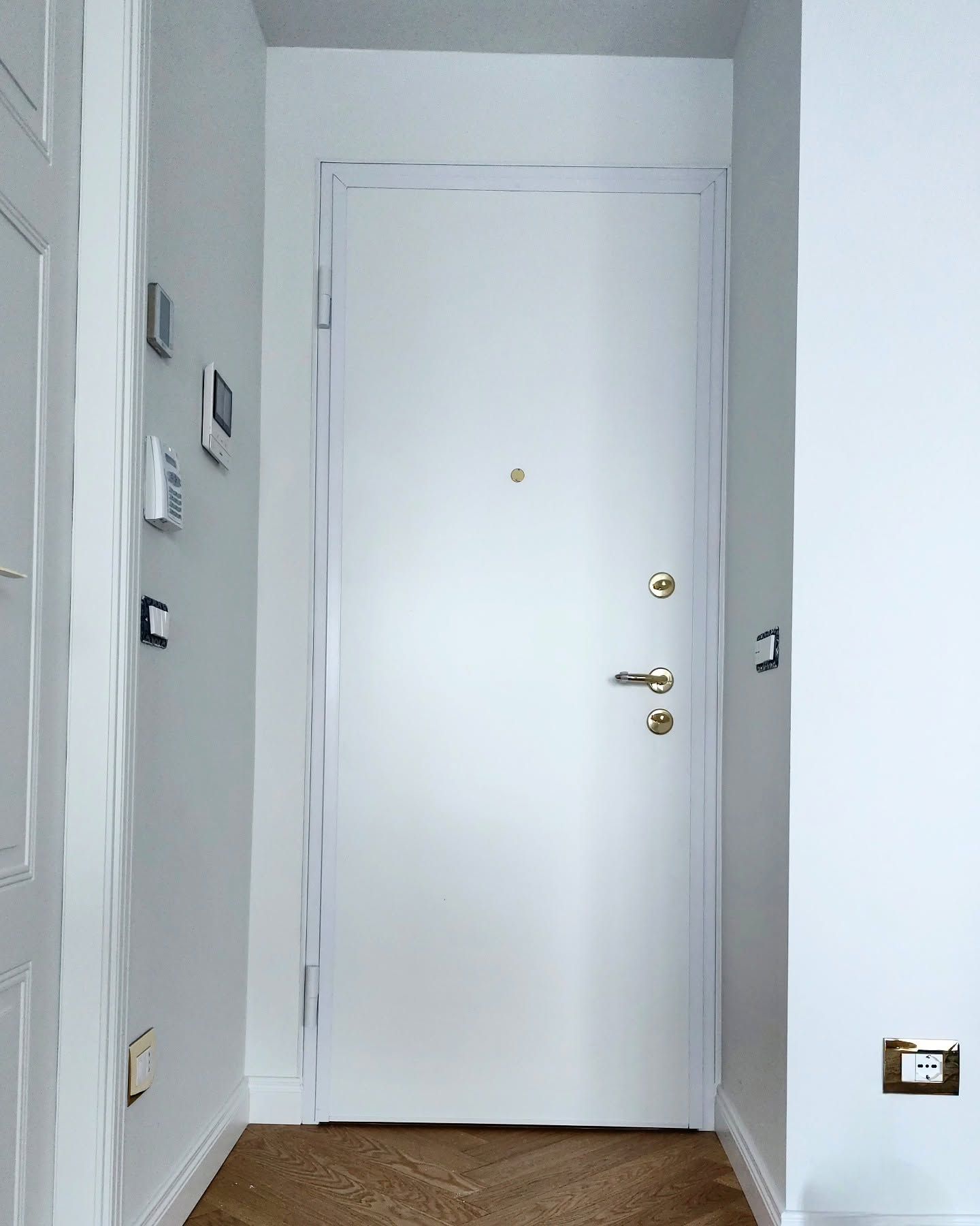 Corridoio stretto con una porta d’ingresso bianca e pareti grigio chiaro, visto dall’interno.