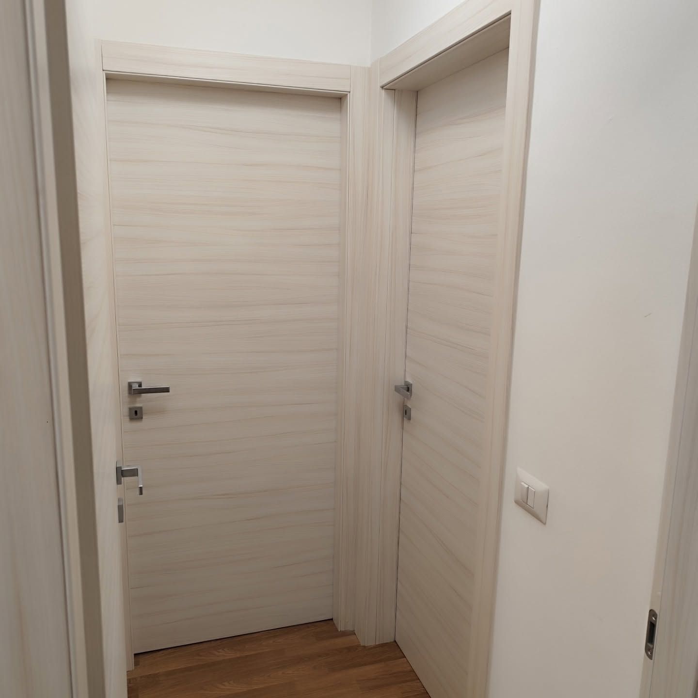 Corridoio stretto con due porte in legno chiaro e pareti bianche, visto dall’interno.