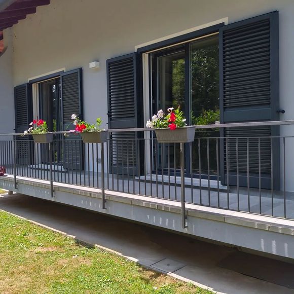 Balcone con persiane e fioriere sulla facciata di una casa grigio chiaro.