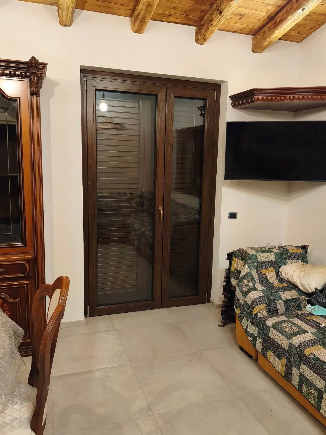 Soggiorno con divano, TV a parete e porte scorrevoli in vetro con cornici in legno, sotto travi a vista sul soffitto