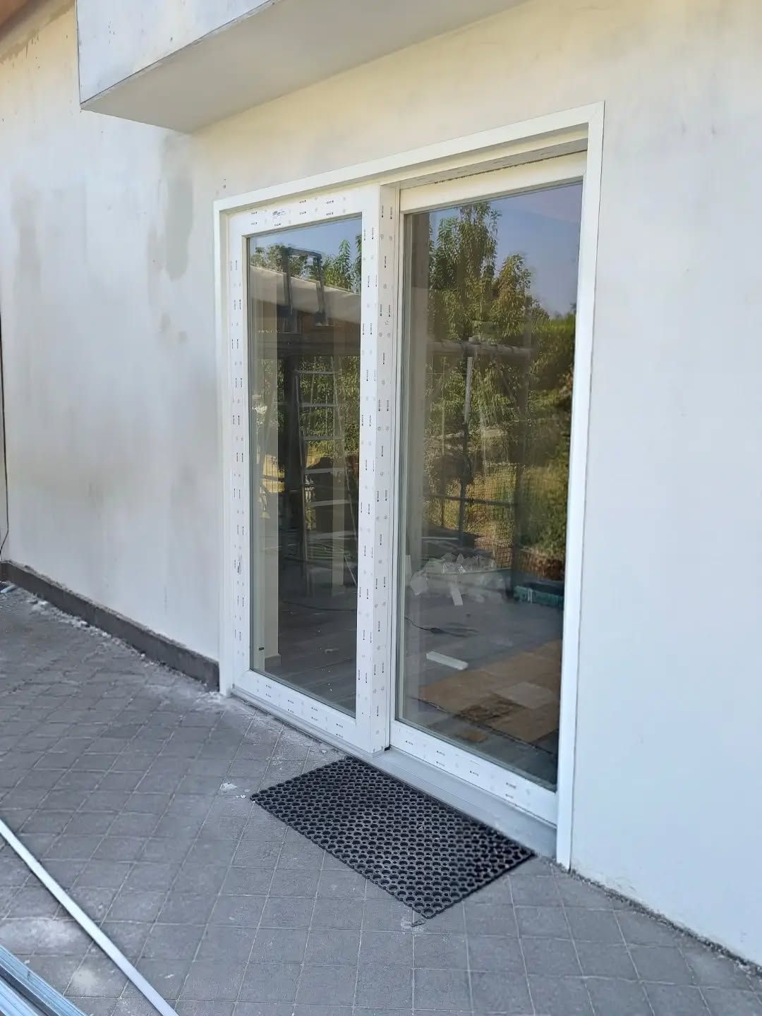 Ingresso con porta scorrevole in vetro, pareti bianche e zerbino su un patio piastrellato.