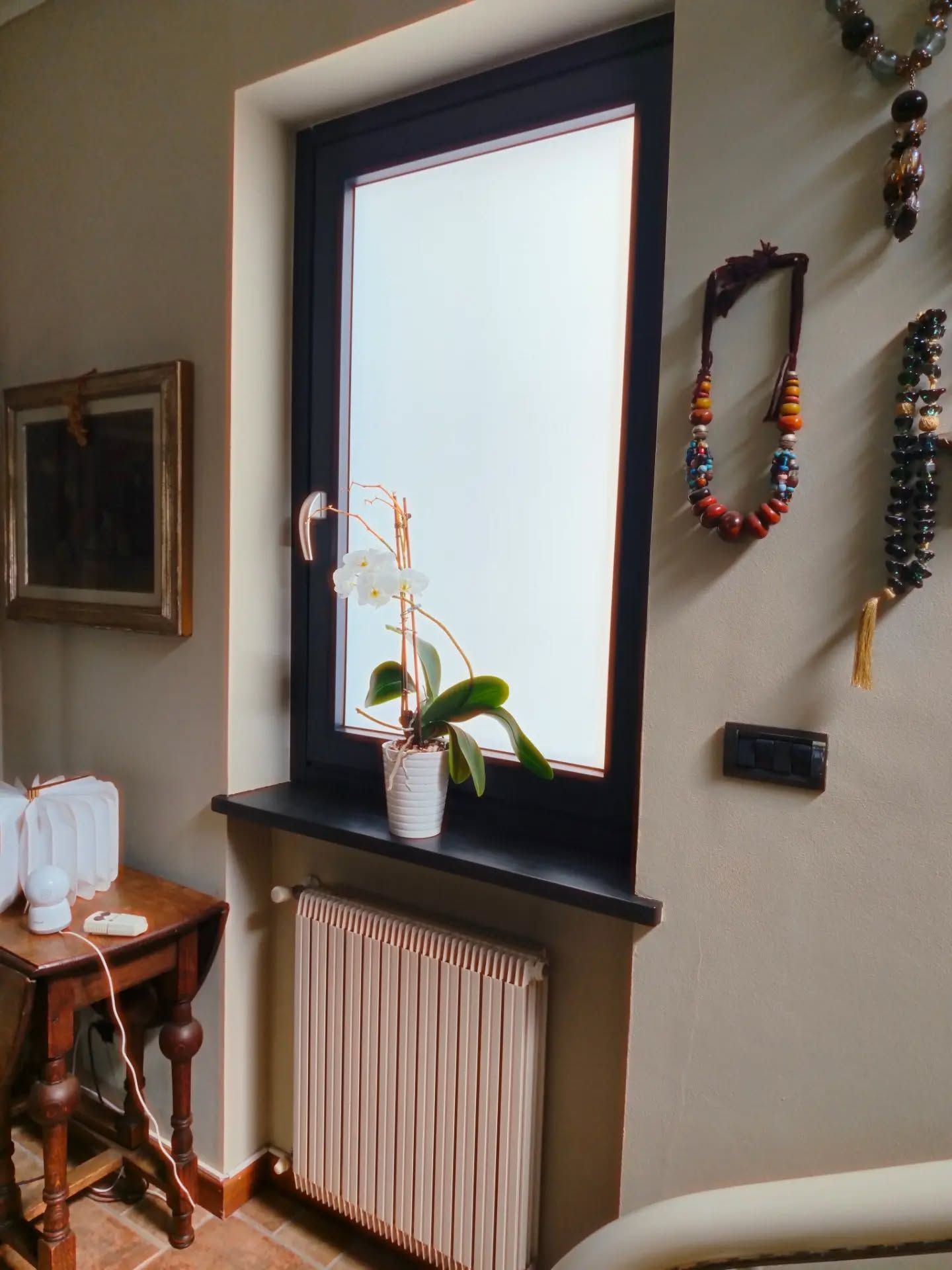 Finestra luminosa con un’orchidea in vaso sul davanzale, sopra un termosifone, in un ambiente accogliente.