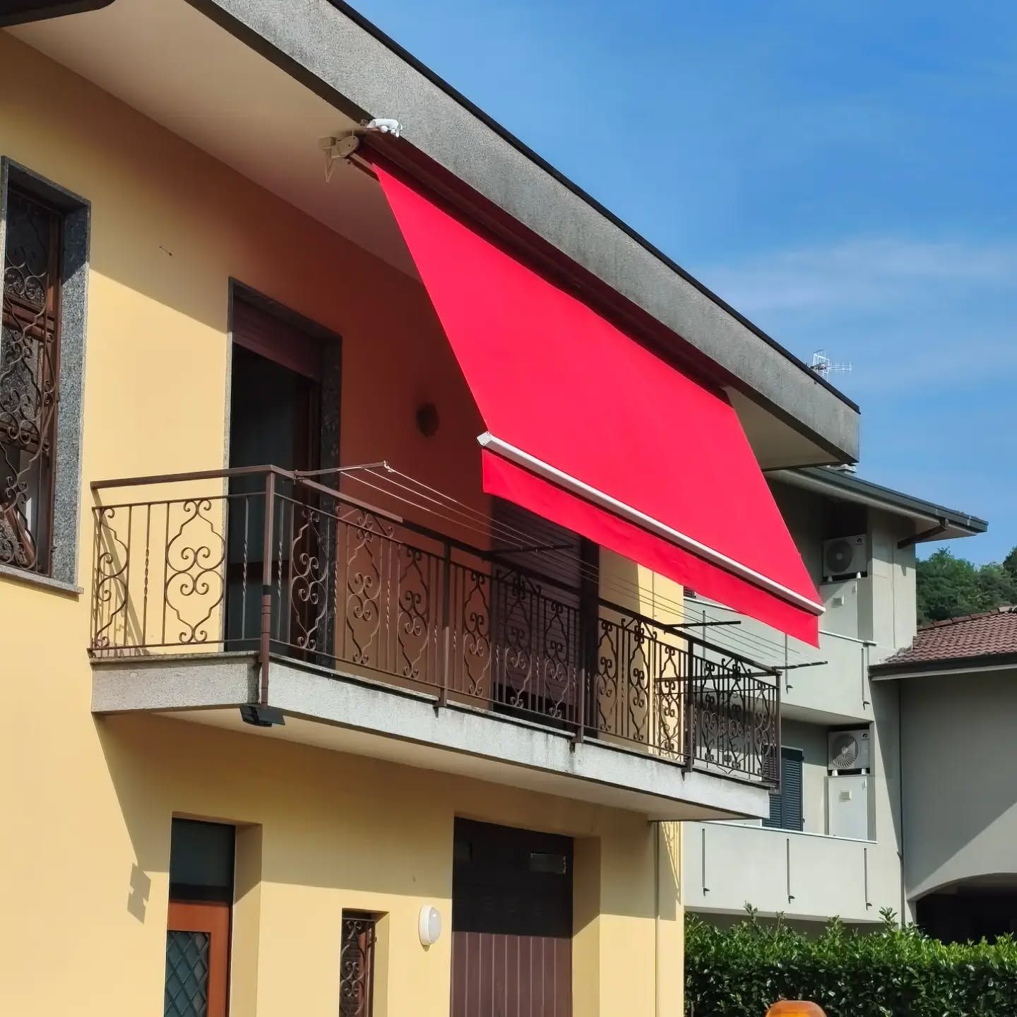 Casa a due piani con una tenda da sole rosso acceso sopra un balcone, in una giornata di sole