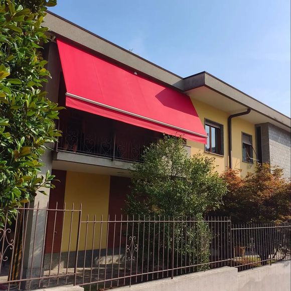 Casa con una tenda da sole rosso vivo, finestre con grate e un cancello davanti, circondata dal verde