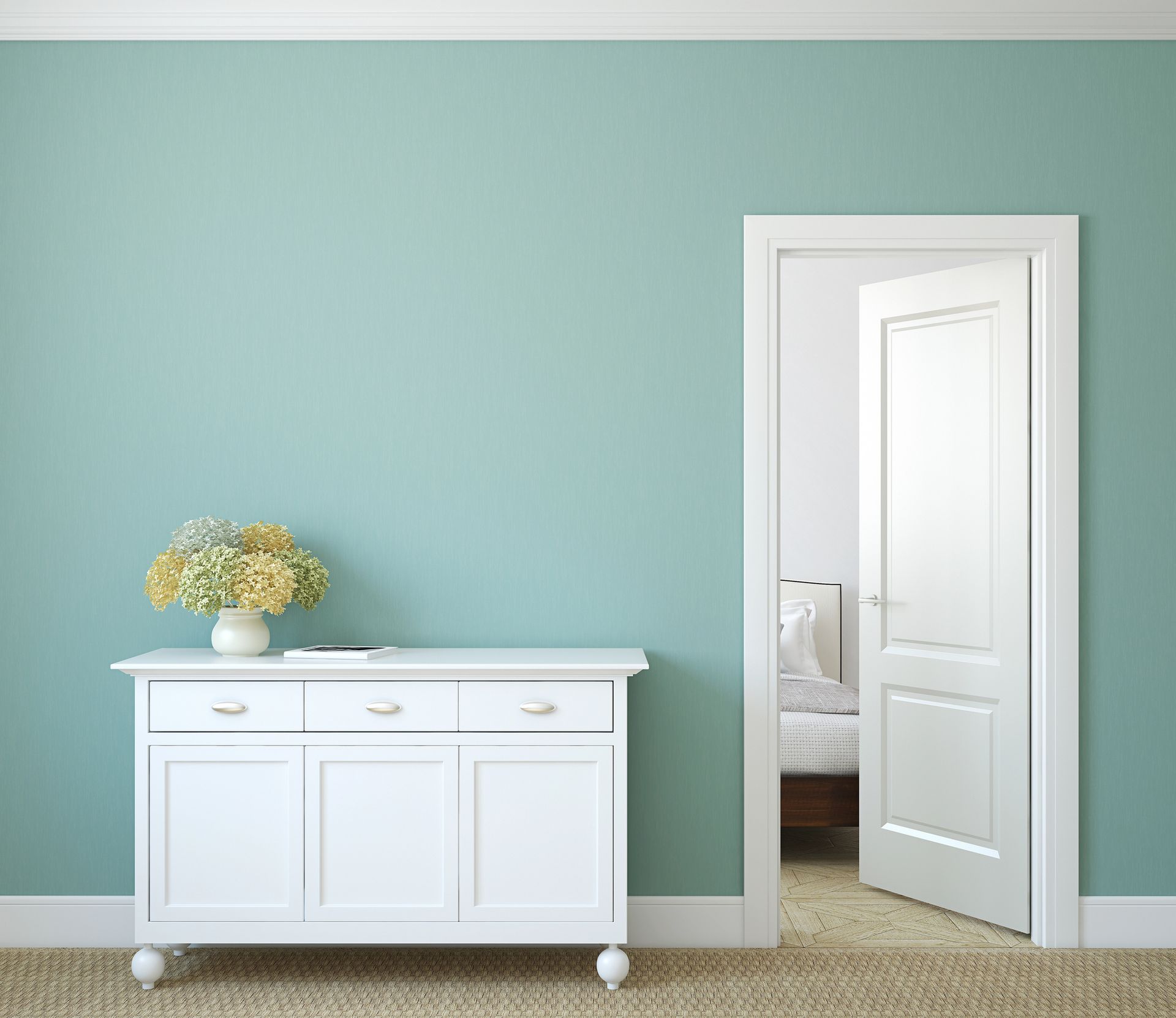 Mobiletto bianco con fiori in una stanza azzurra, accanto a una porta aperta.