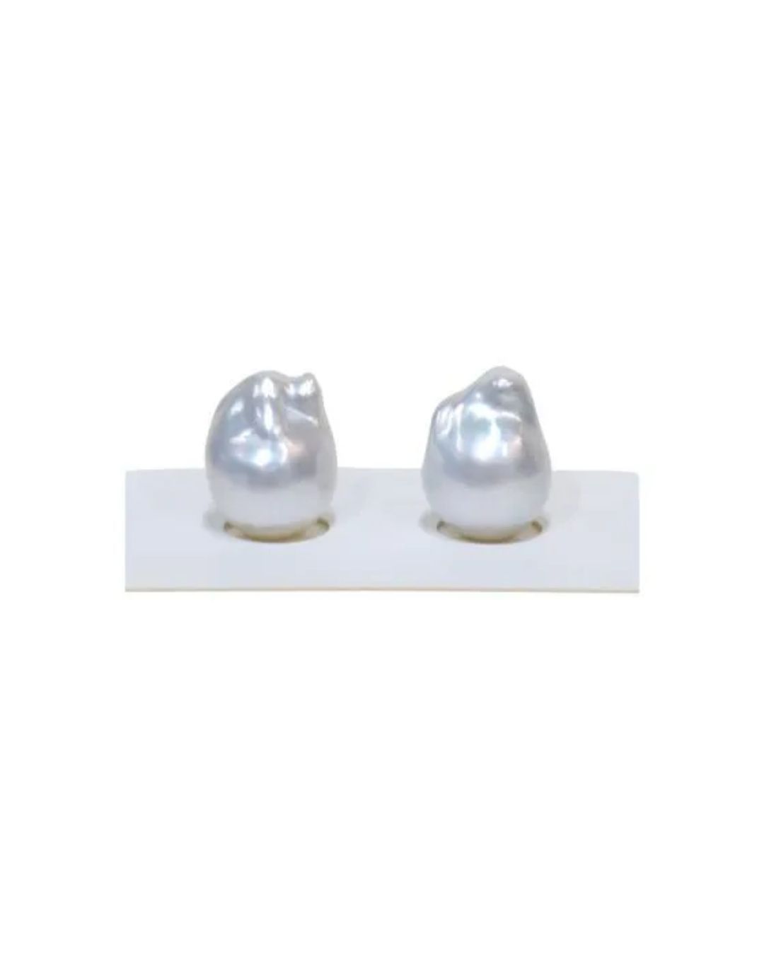 Two large, irregular white baroque pearls sitting on a white display stand against a white background.