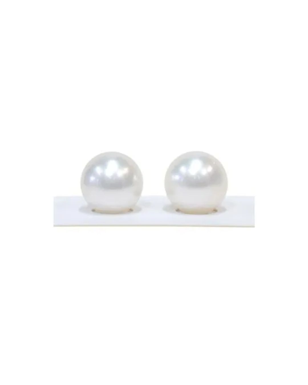 Two lustrous, spherical white pearls displayed side-by-side on a small, white rectangular base.