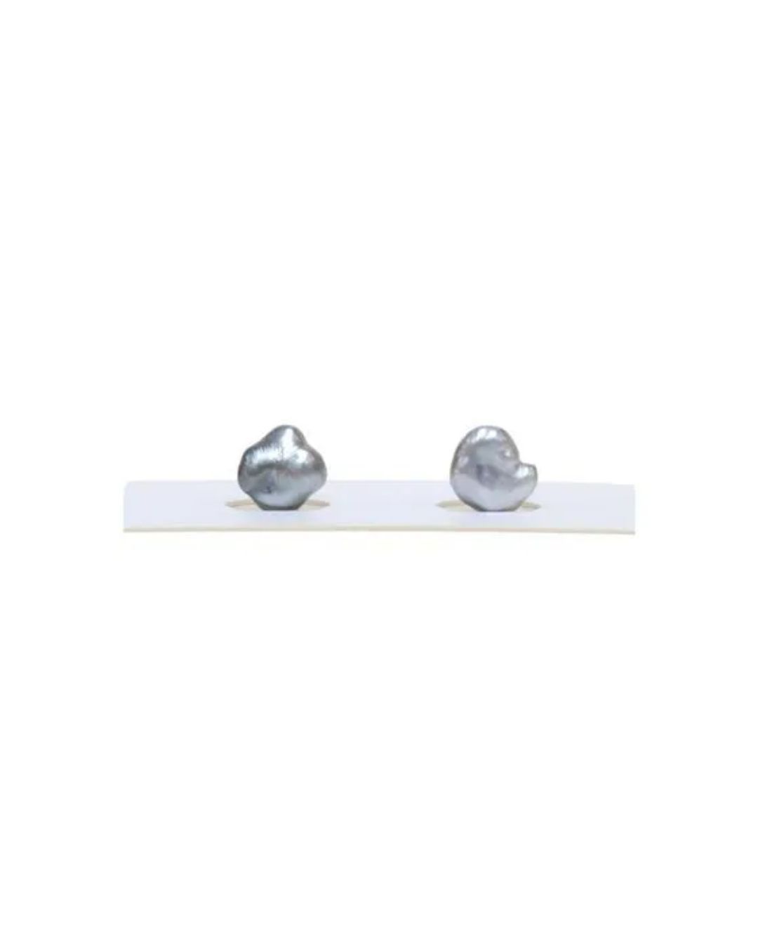 Two gray, irregularly shaped baroque pearls resting in circular indentations on a white display strip.