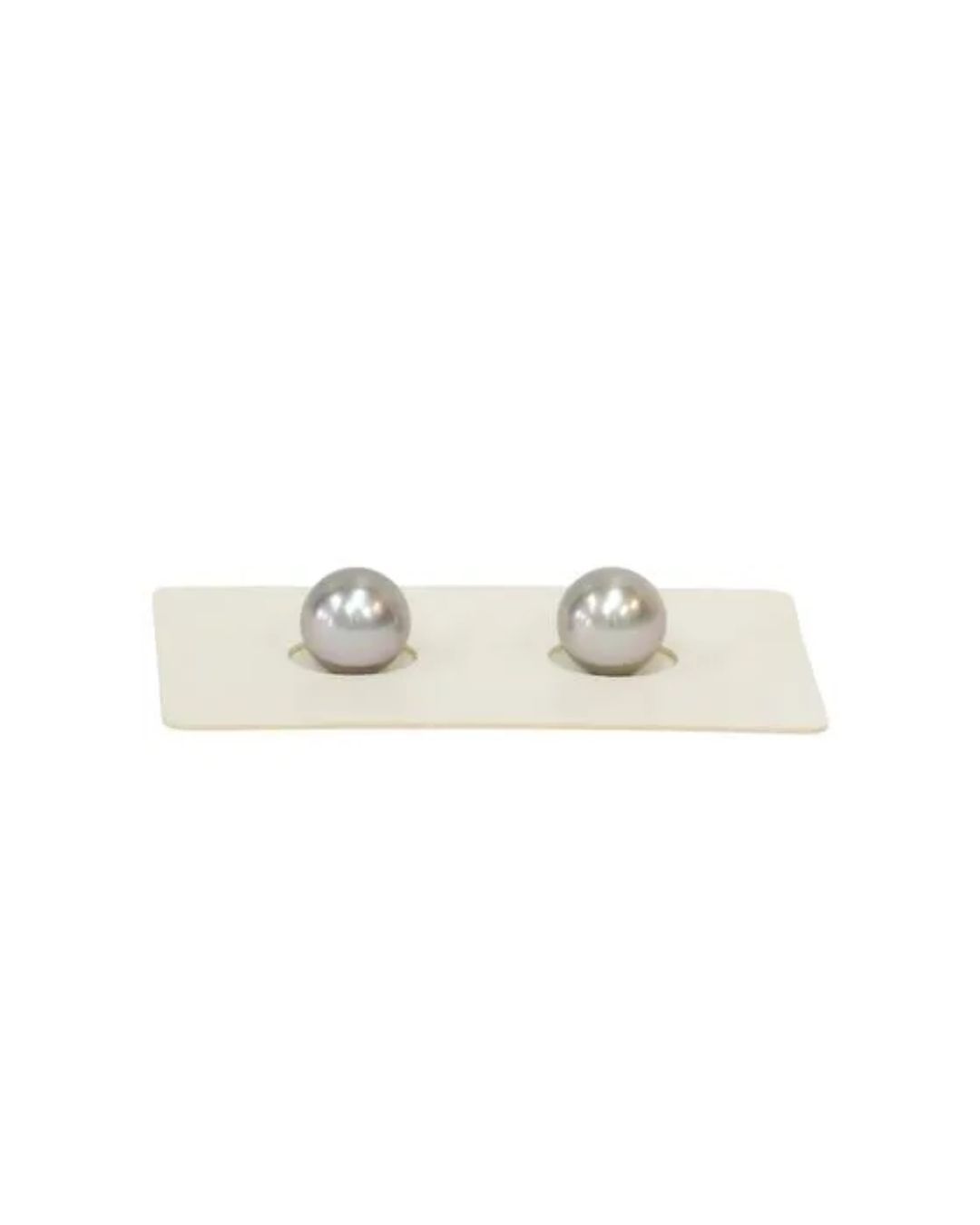 Two lustrous, light gray spherical pearls sit side-by-side in circular indentations on a white rectangular display card.
