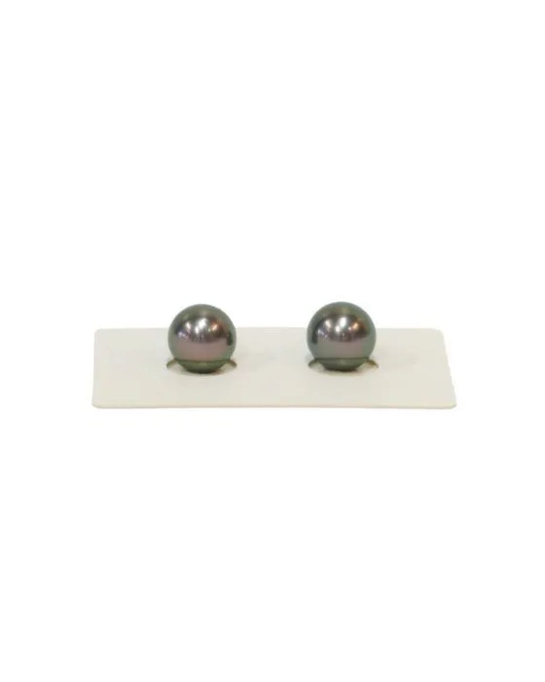 Two dark, spherical pearls sit side-by-side in circular cutouts on a small, rectangular white display card.