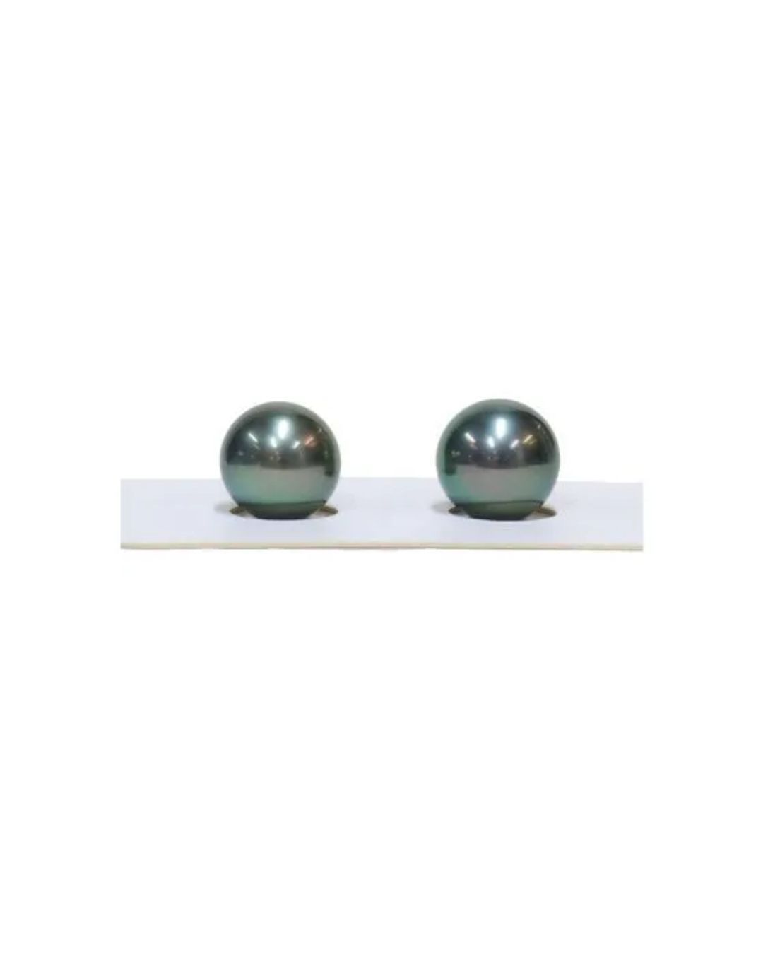 Two round, iridescent dark peacock-green pearls sitting on a white display card with circular cutouts.