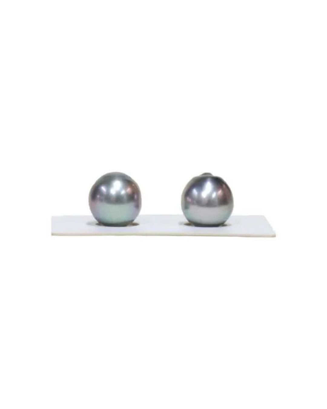 Two lustrous, dark gray-toned pearls sit side-by-side on a small, white display stand against a white background.