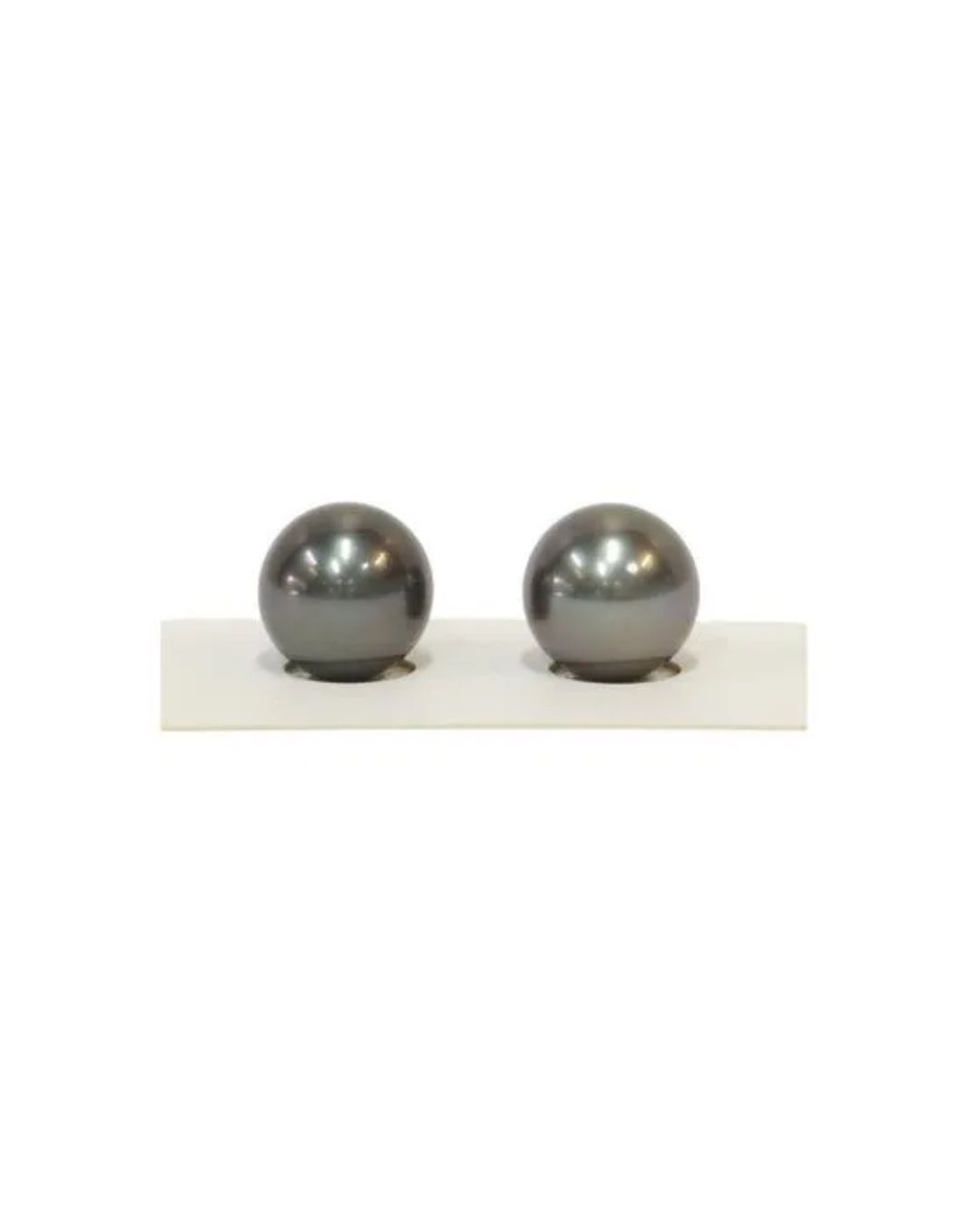 Two lustrous, dark gray round pearls sitting side-by-side in a white display holder.
