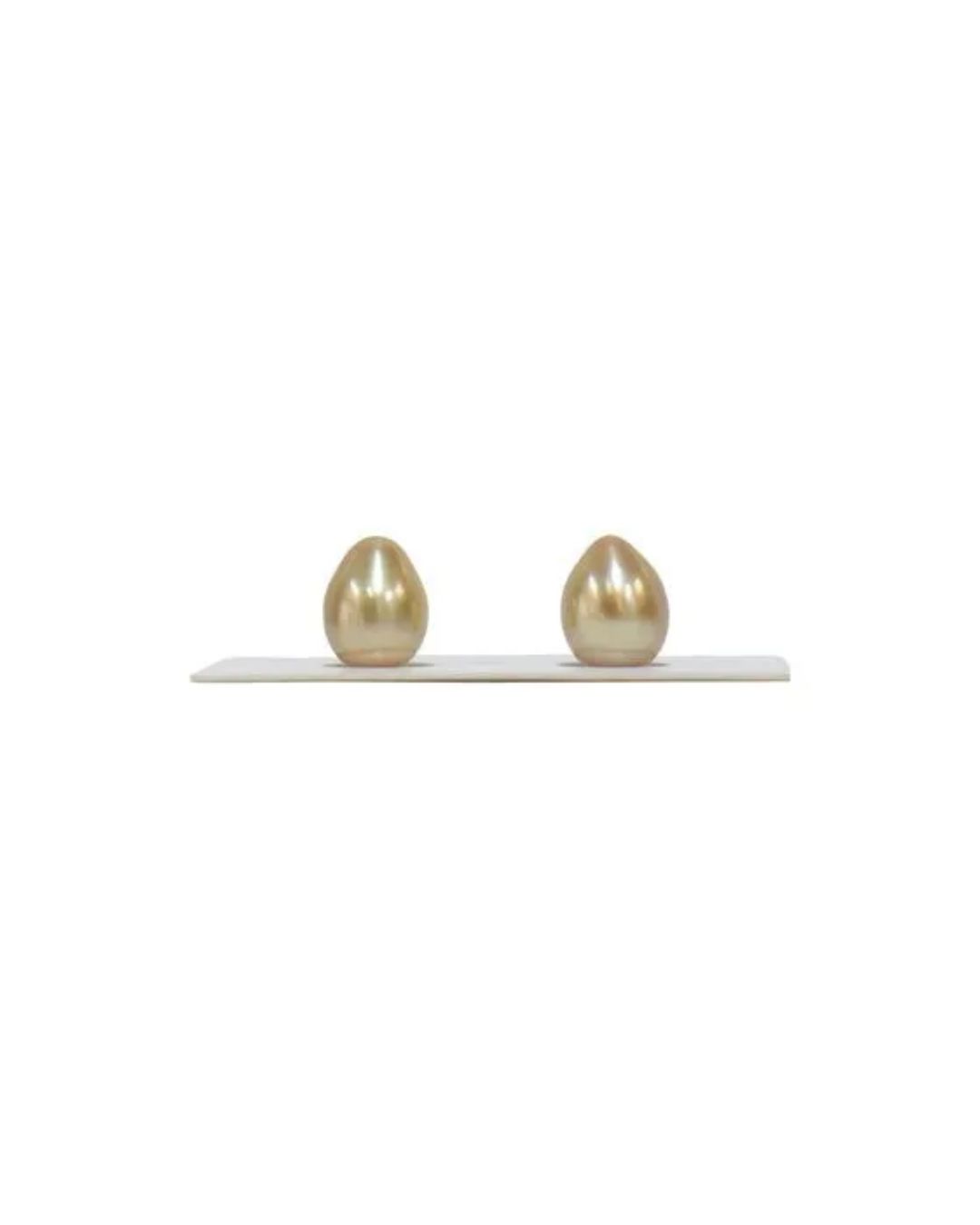 Two drop-shaped, golden-colored pearls sitting upright on a white display strip against a white background.
