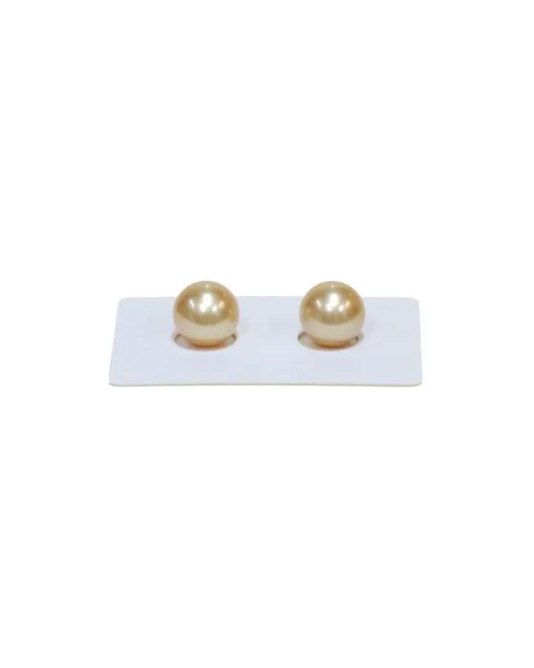 Two golden-hued spherical pearls displayed side-by-side on a small, rectangular white stand.