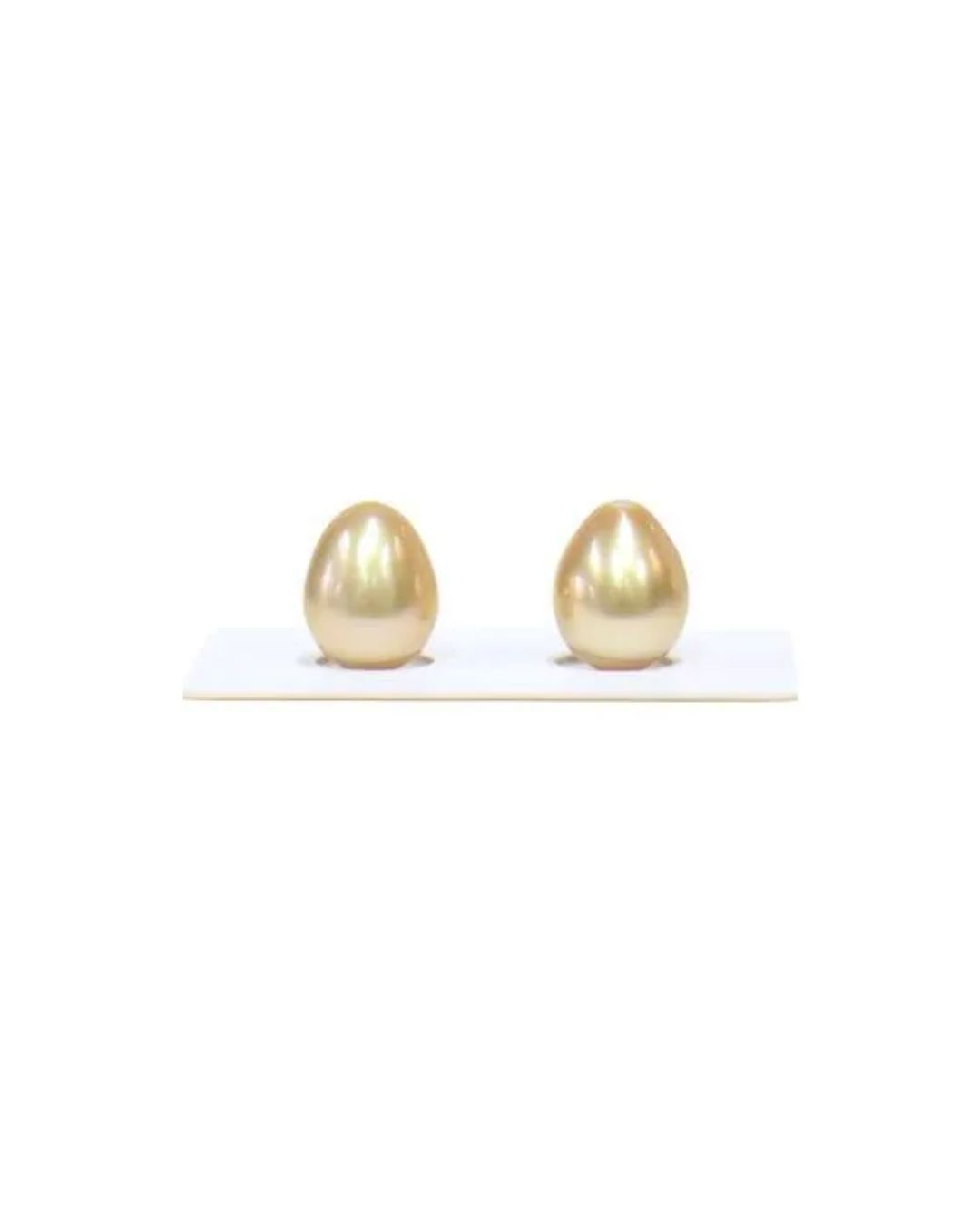 Two metallic, gold-colored, egg-shaped pearls stand upright in a white display tray against a plain white background.