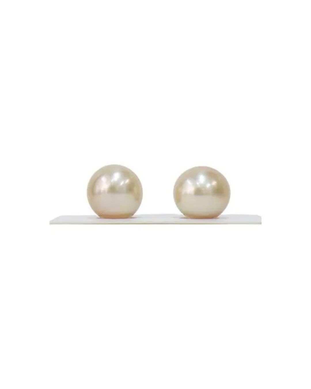 Two round, champagne-colored pearls resting side-by-side on a thin white surface against a plain white background.