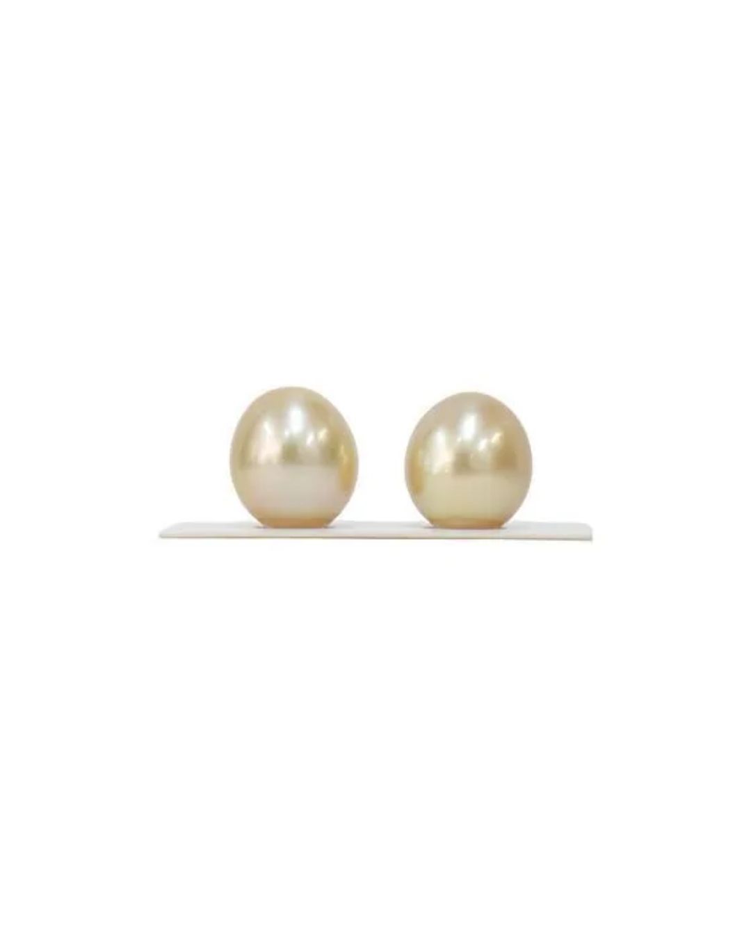 Two lustrous, golden-hued, teardrop-shaped pearls displayed side-by-side on a slim white base against a white background.
