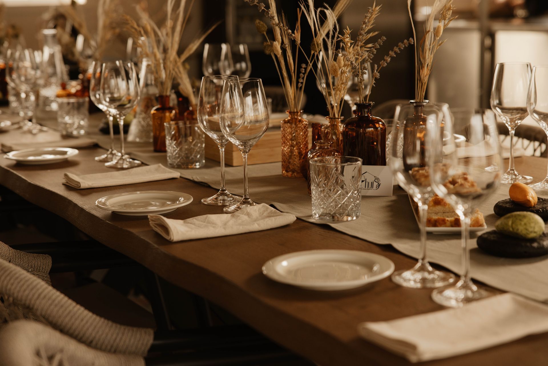 Een elegante eettafel gedekt met witte borden, glaswerk, kaarsen en gedroogde bloemen als tafeldecoratie.