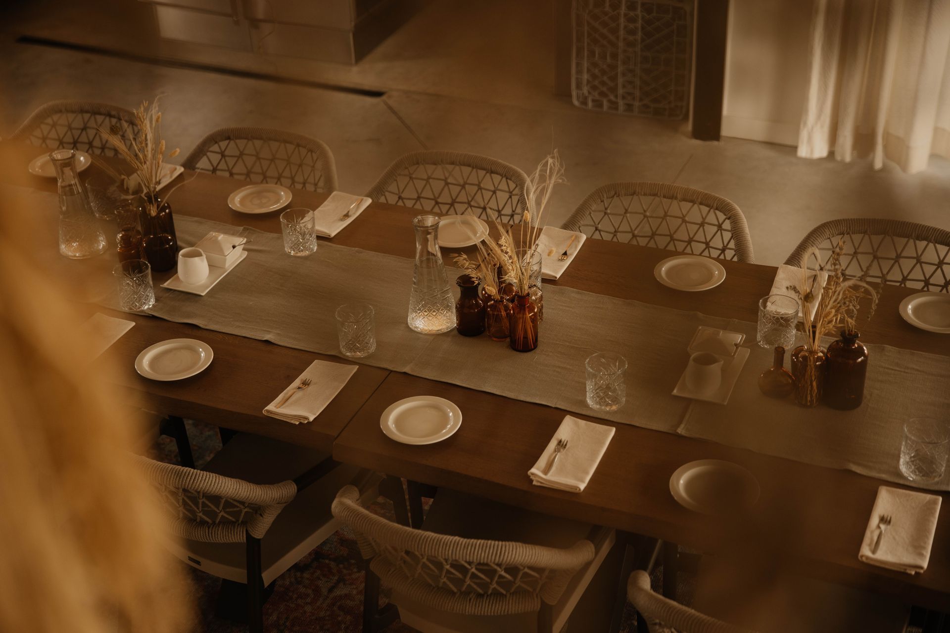 Een sfeervol verlichte restauranttafel, gedekt met borden, menukaarten en rieten stoelen, in een warmbruin interieur.