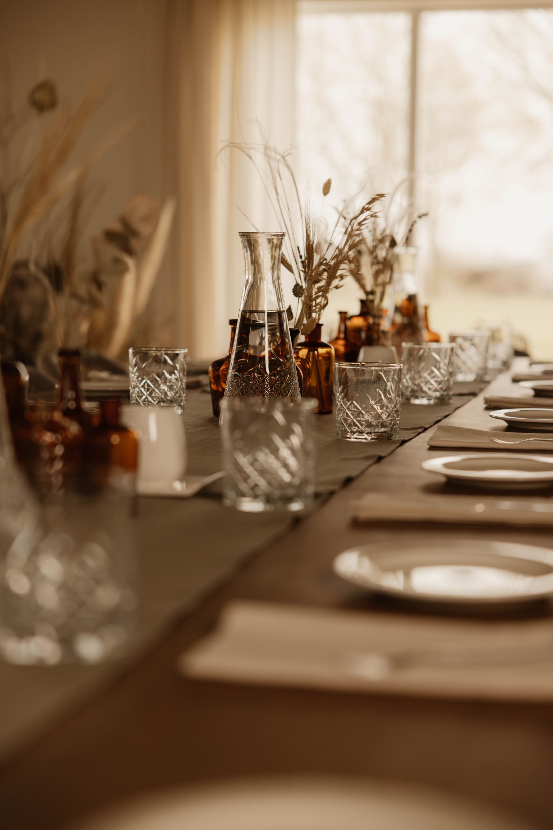 Een elegante eettafel gedekt met glaswerk, borden en gedroogde bloemen in een sfeervol licht.