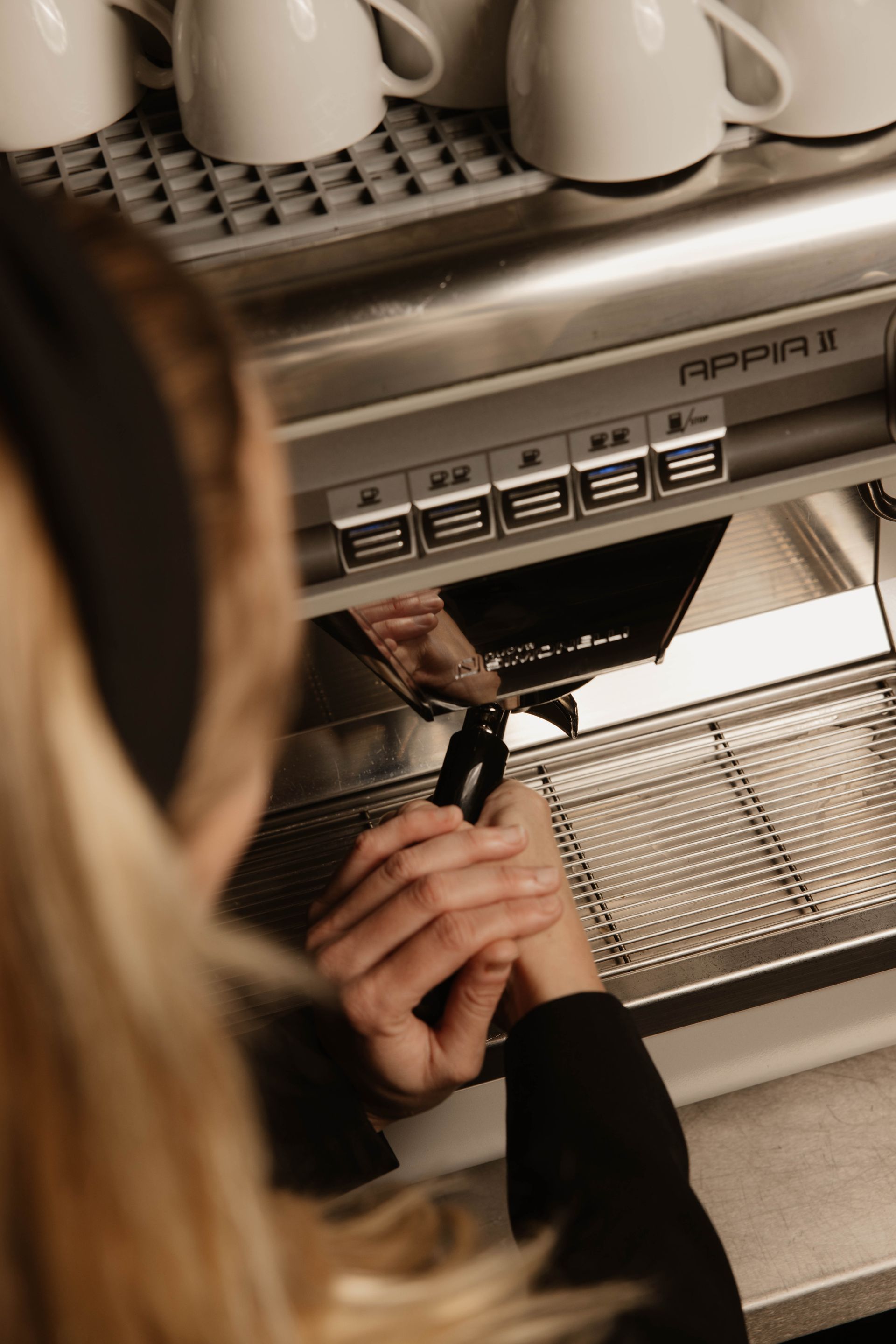 Iemand gebruikt een espressomachine en houdt een portafilter onder de dispenser.