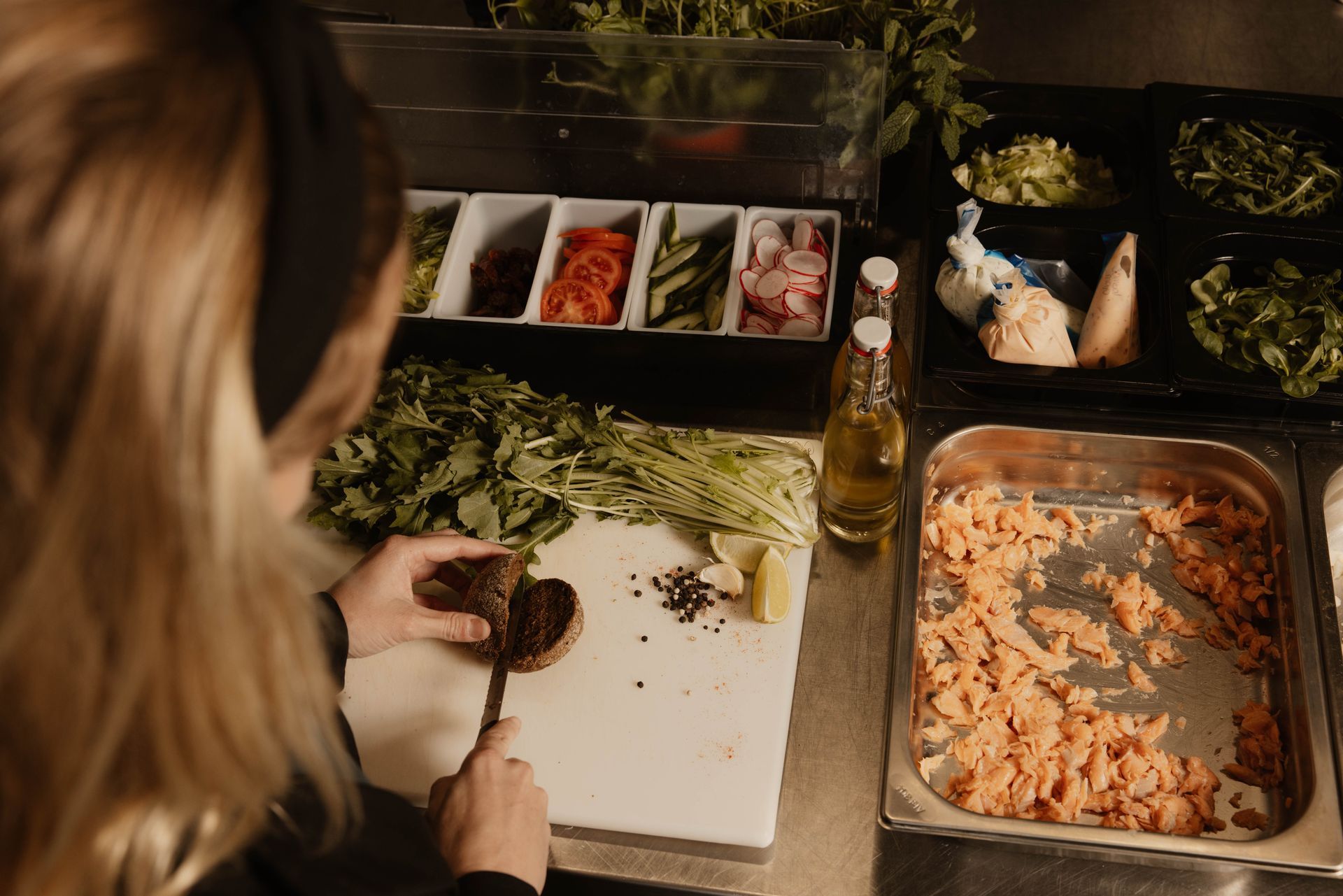 Iemand die een saladebar klaarmaakt met sla, toppings en flesjes dressing op een toonbank.
